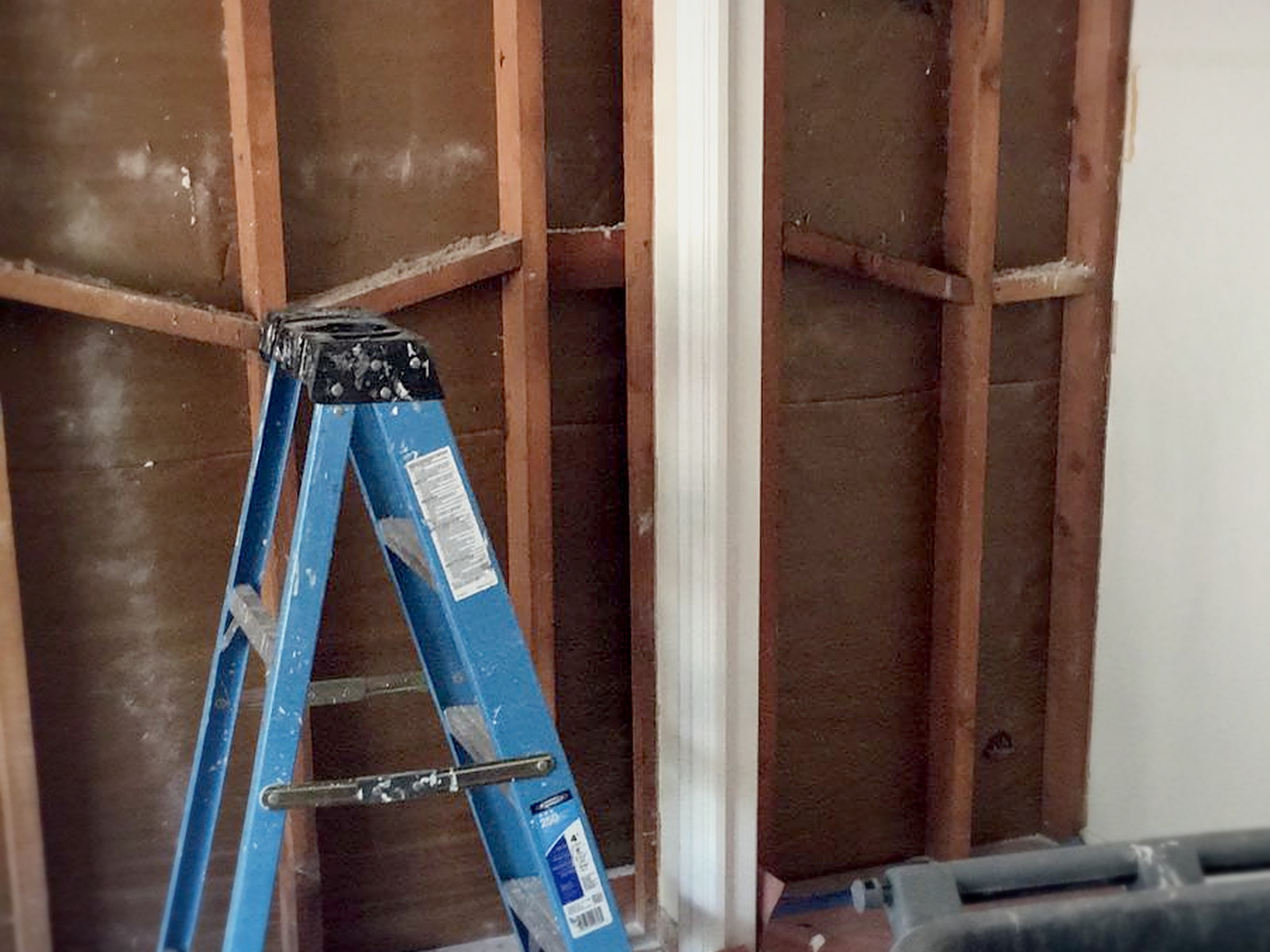 Melrose residential wall stripped to bare studs with a step ladder and debris bin before soundproofing