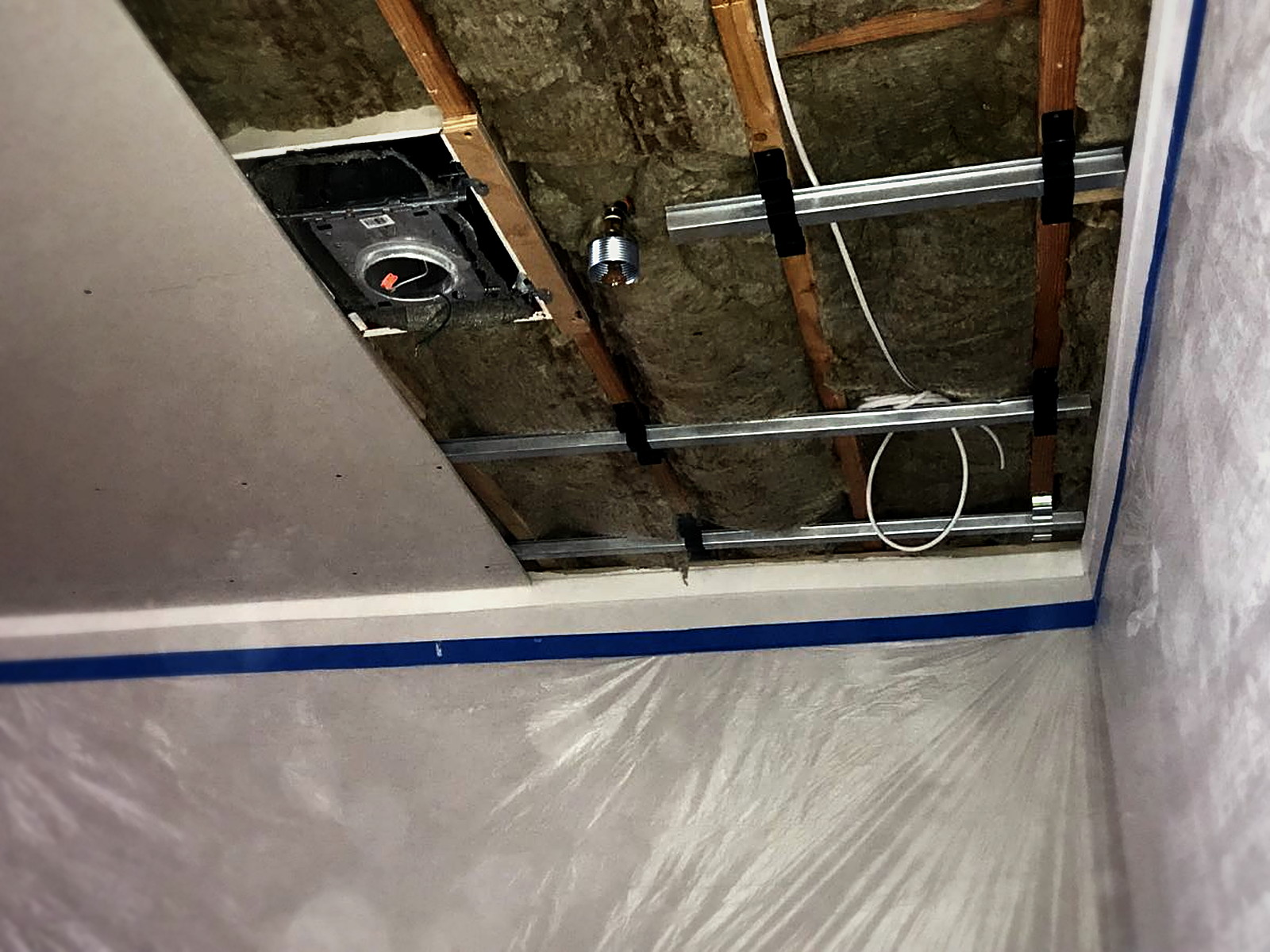 Close view of isolation clips carrying hat channel beneath insulated joists next to finished drywall