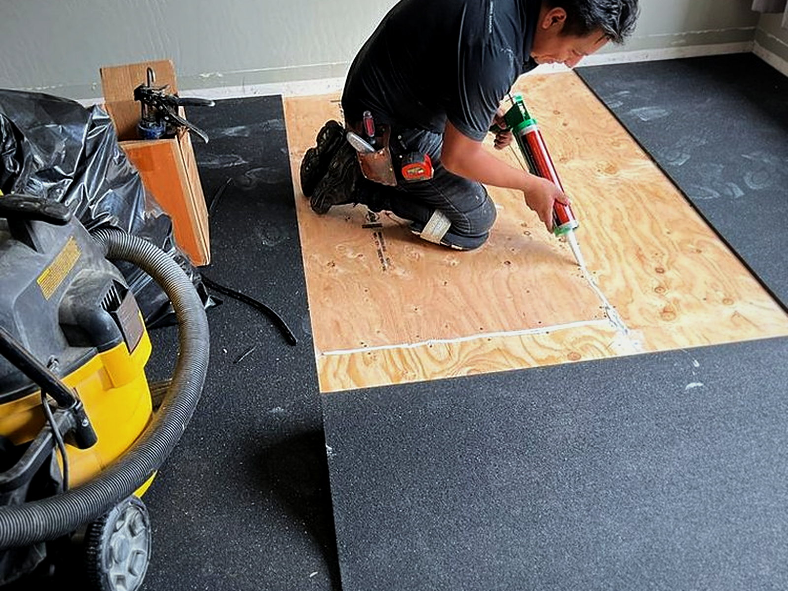 Installer applying acoustic sealant along a plywood seam before Serenity acoustic underlay is rolled out