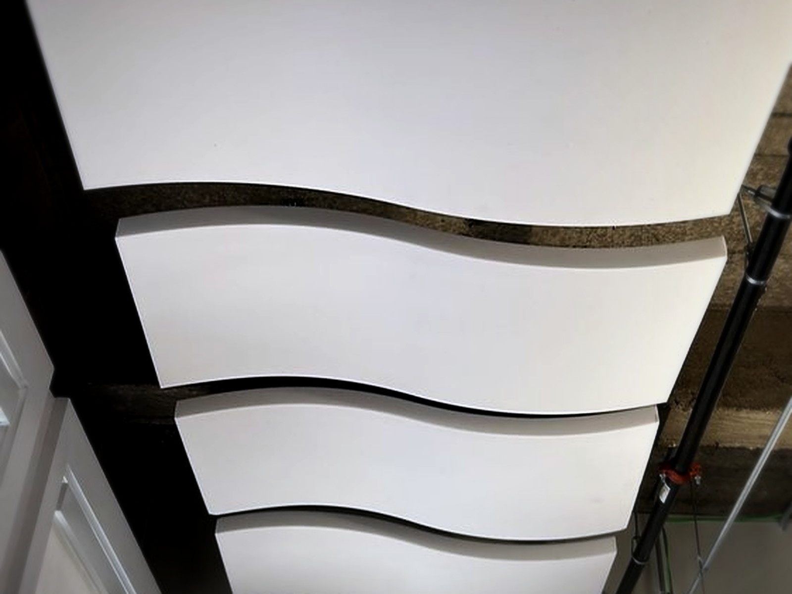 Close view of four white wave acoustic clouds spaced evenly under an exposed wood beam ceiling