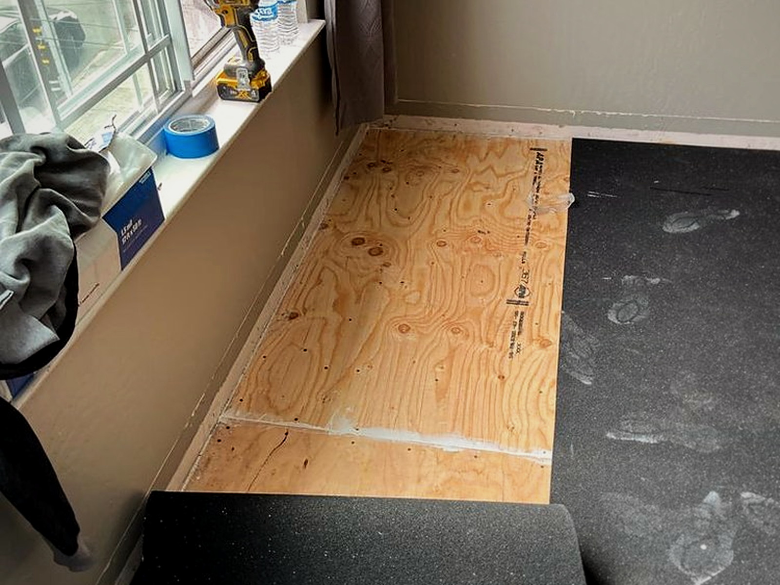 Serenity acoustic underlay cut around a window wall with the plywood subfloor still exposed at the perimeter