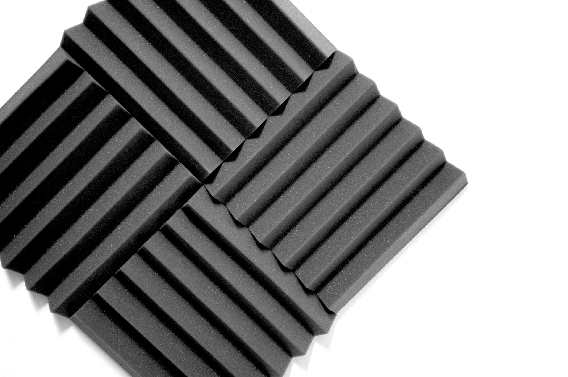 Four charcoal wedge acoustic foam panels arranged on a white background — acoustics basics.