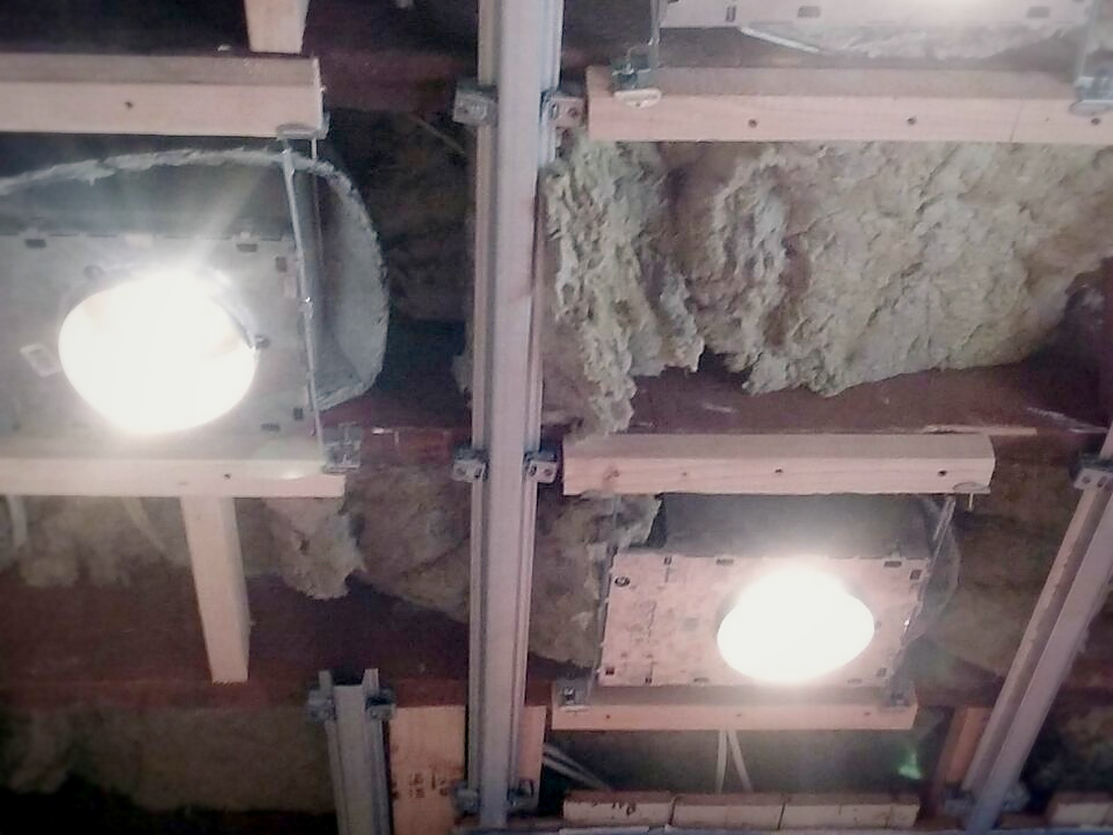 Fire-rated recessed light covers installed over downlights in an insulated ceiling before drywall