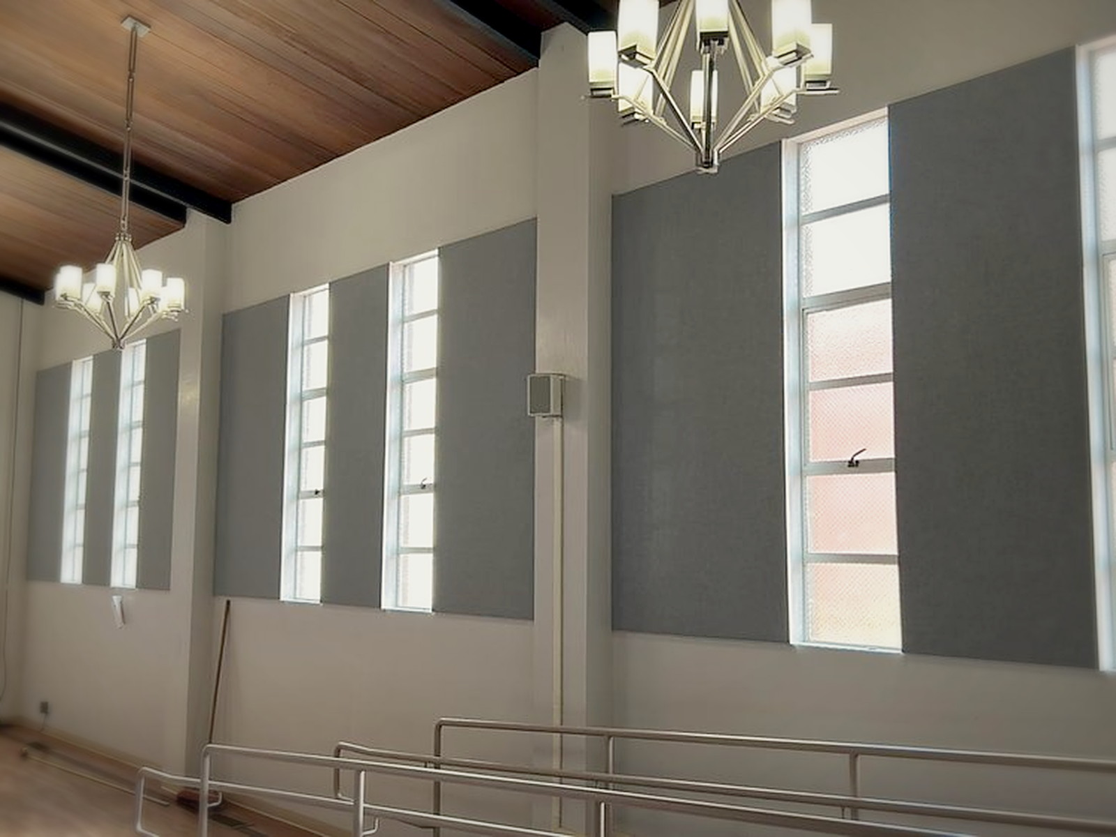 Wide view of finished grey custom fabric track panels running between window bays under a vaulted wood ceiling