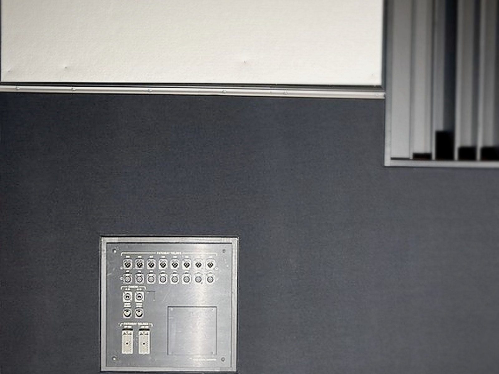 Recording studio wall plate for audio tie-lines set flush into charcoal fabric-wrapped acoustic wall panels
