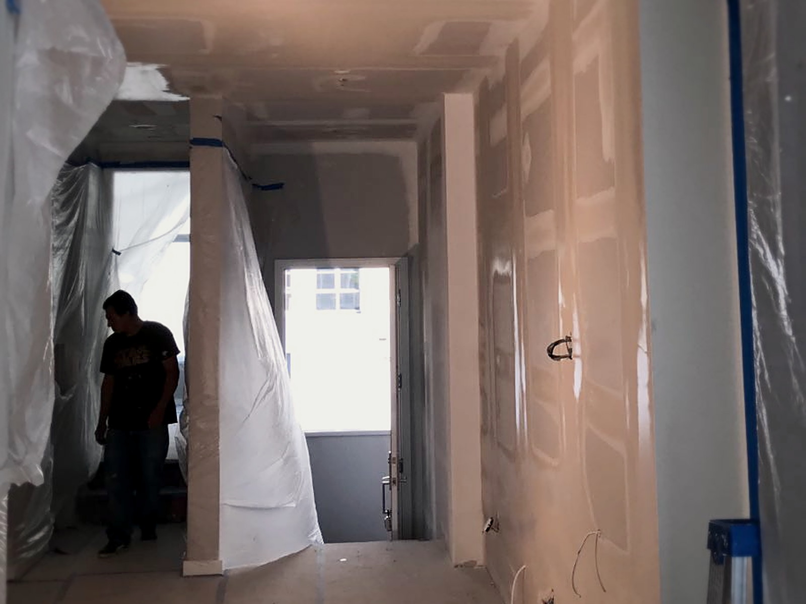 Taped and mudded soundproofed ceiling and walls in a San Francisco residential hallway under plastic protection