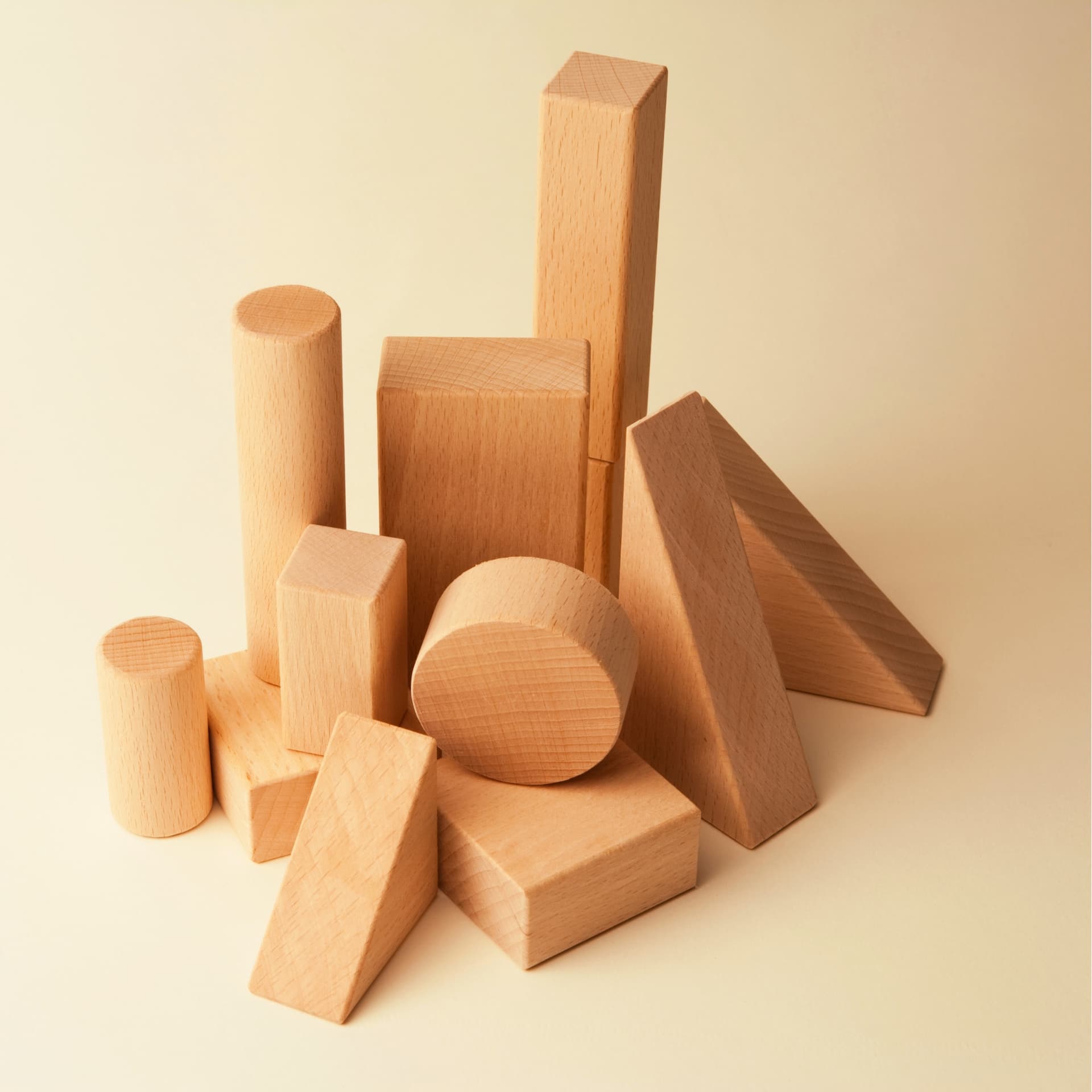 Assorted natural wood building blocks stacked on a cream backdrop — soundproofing basics.