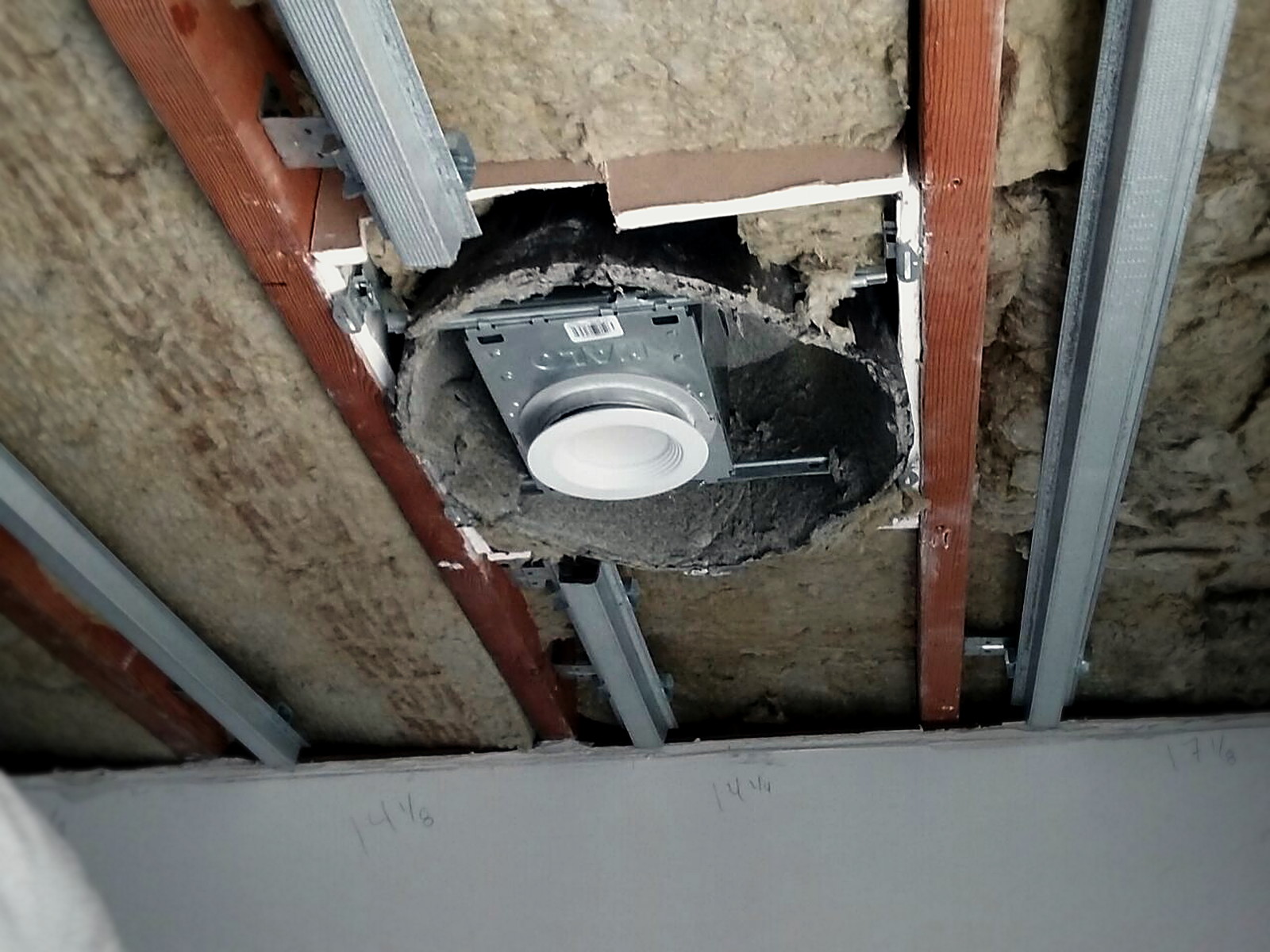 Recessed light housing detailed and boxed within an insulated classroom ceiling before drywall