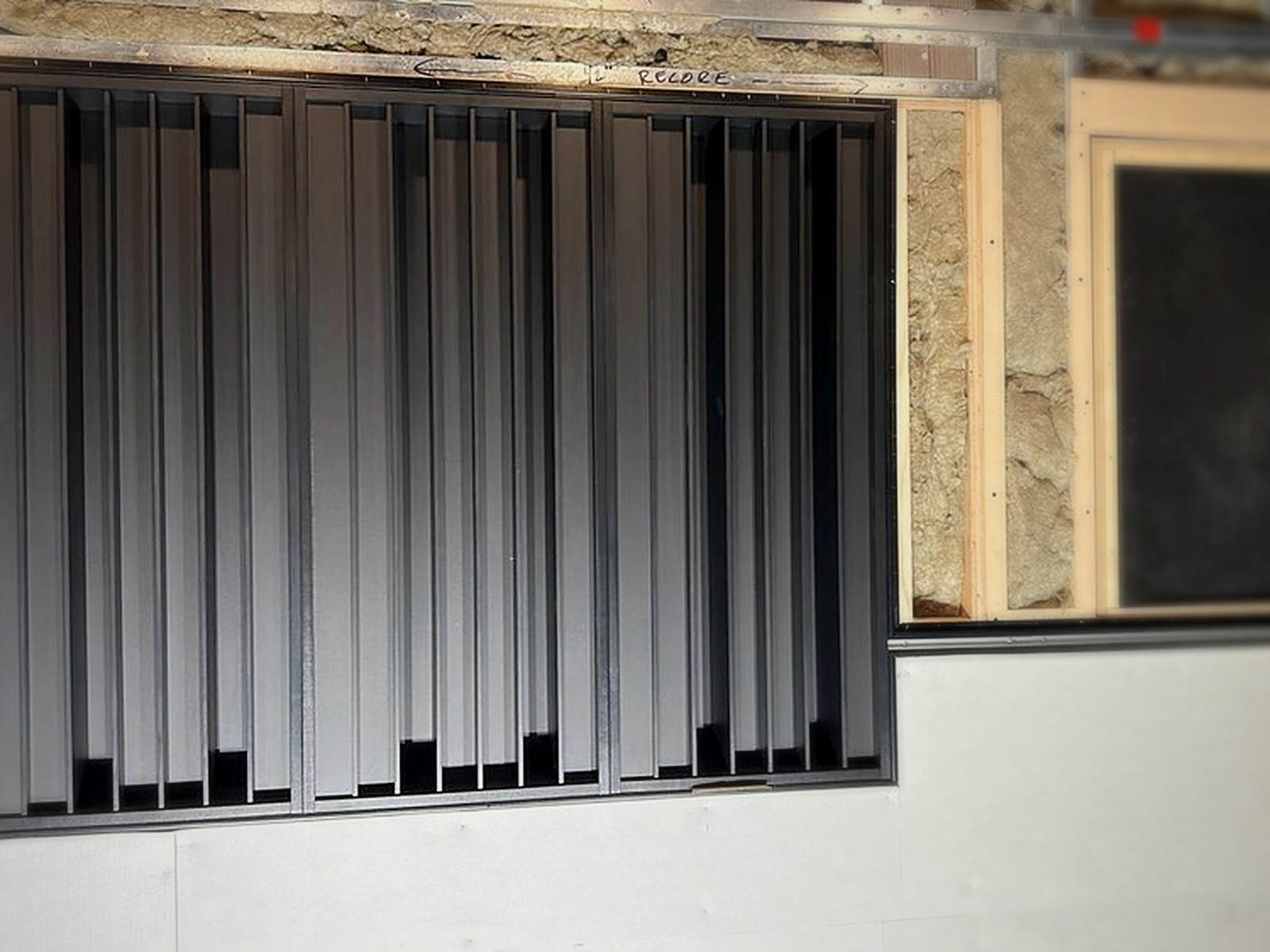 Black slat diffuser bay installed in an open wall frame with mineral wool insulation visible behind
