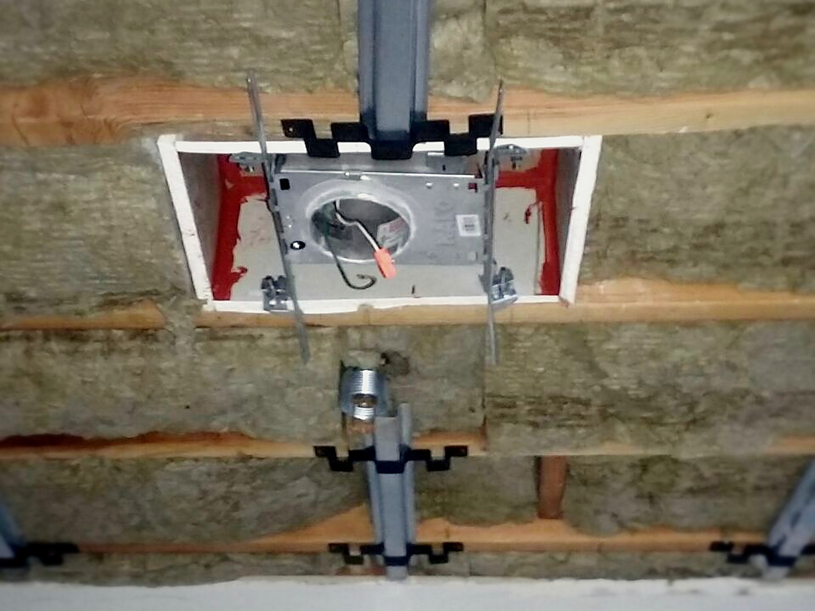 Mineral wool insulation packed between ceiling joists around a recessed light housing and hat channel