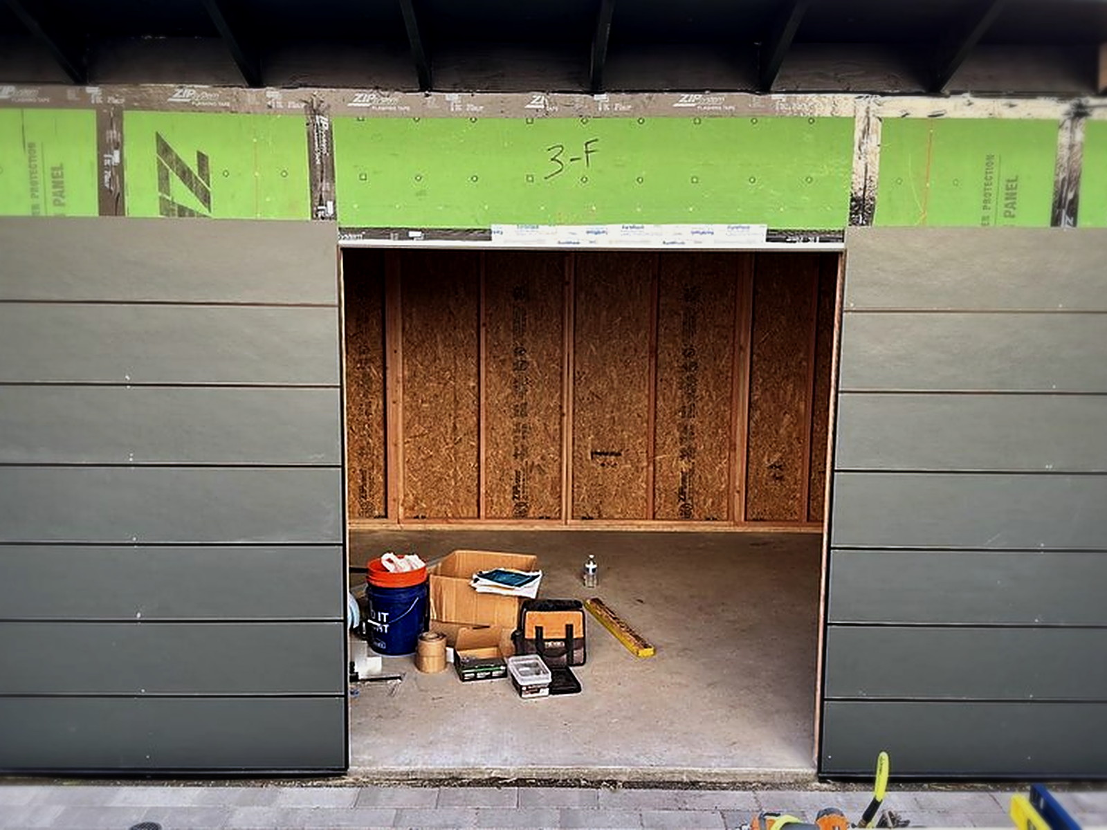 Soundproof studio shed exterior with gray fiber cement siding panels installed over green ZIP System sheathing