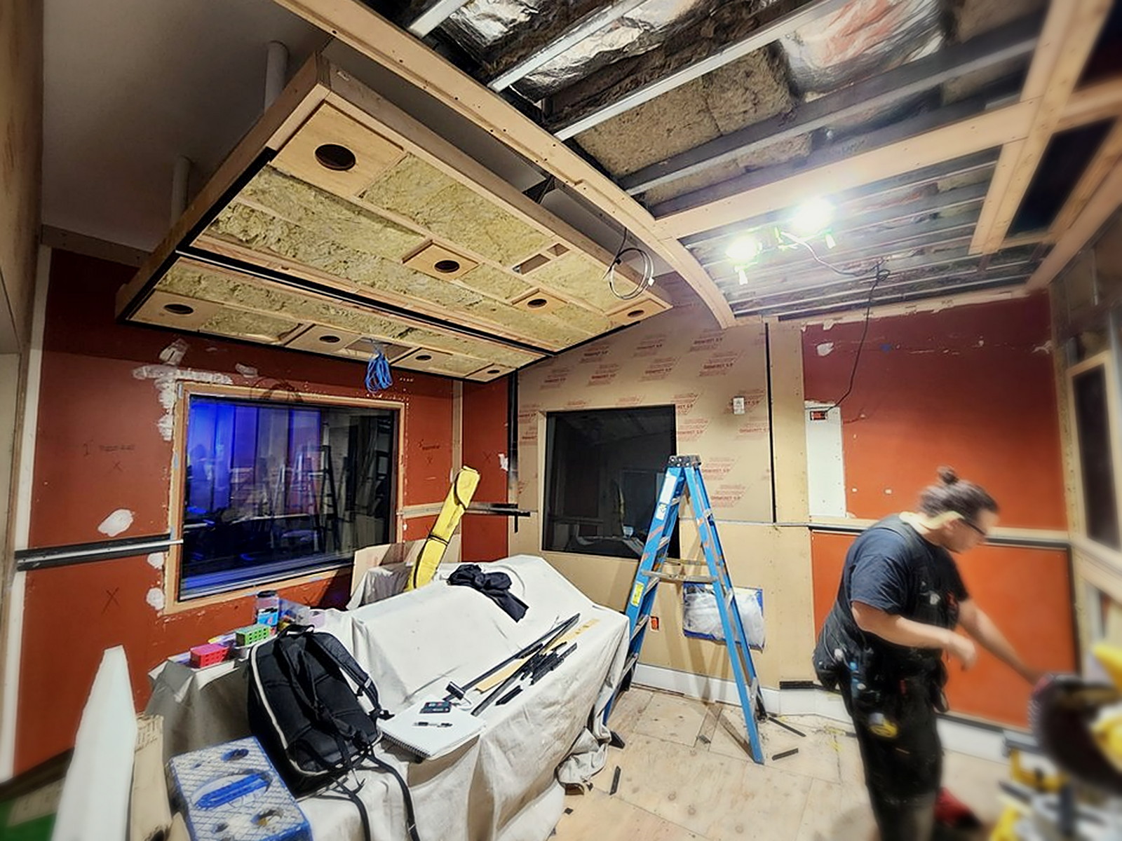 San Francisco recording studio during demolition with exposed ceiling framing, orange walls, ladders and crew at work