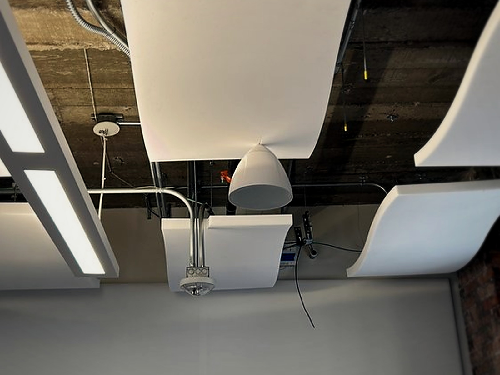 Acoustic wave clouds installed around pendant lighting, a sprinkler head and ceiling fixtures in an office conference room