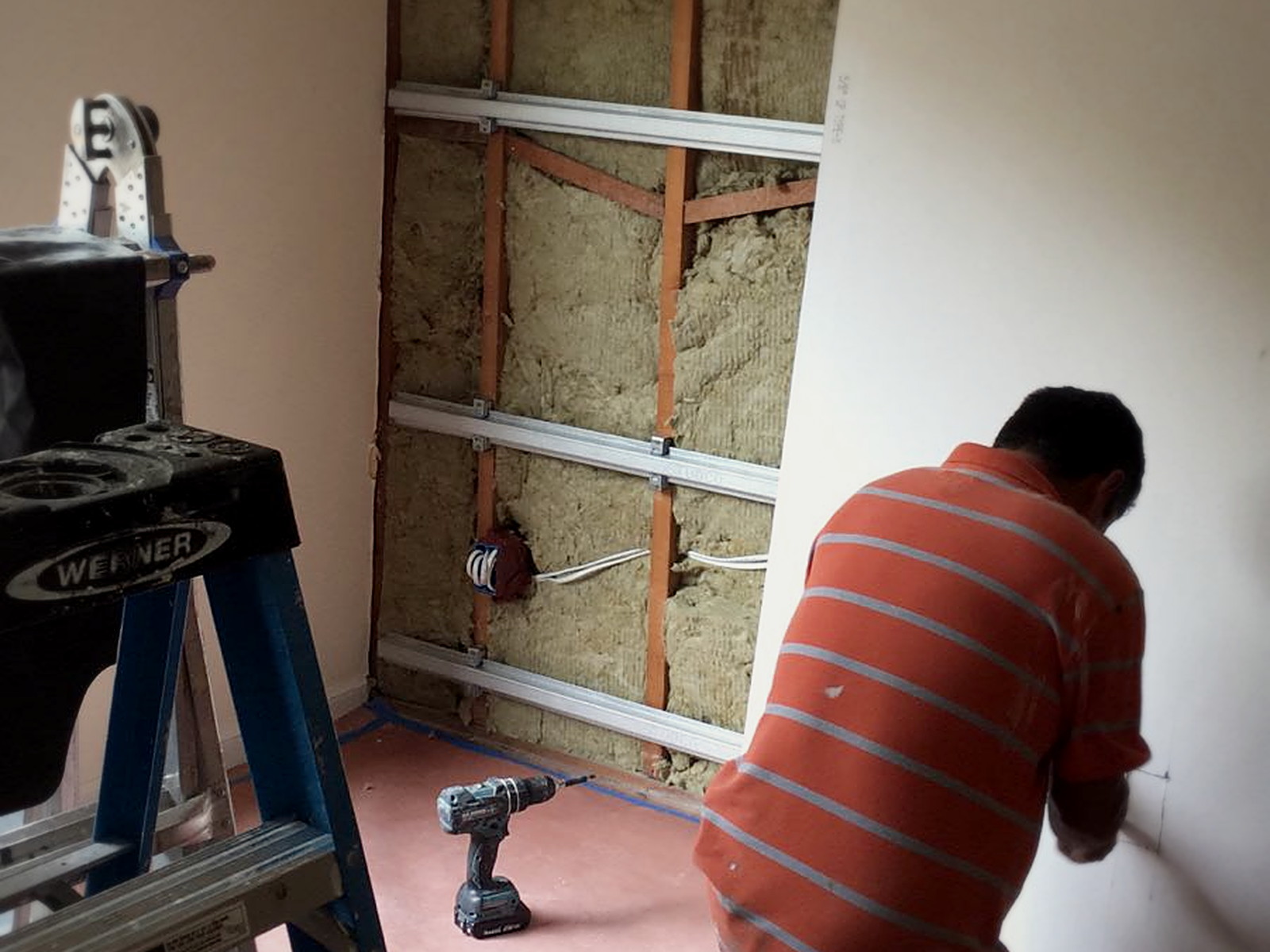 Classroom wall opened to studs with mineral wool insulation and isolation clips carrying metal channel