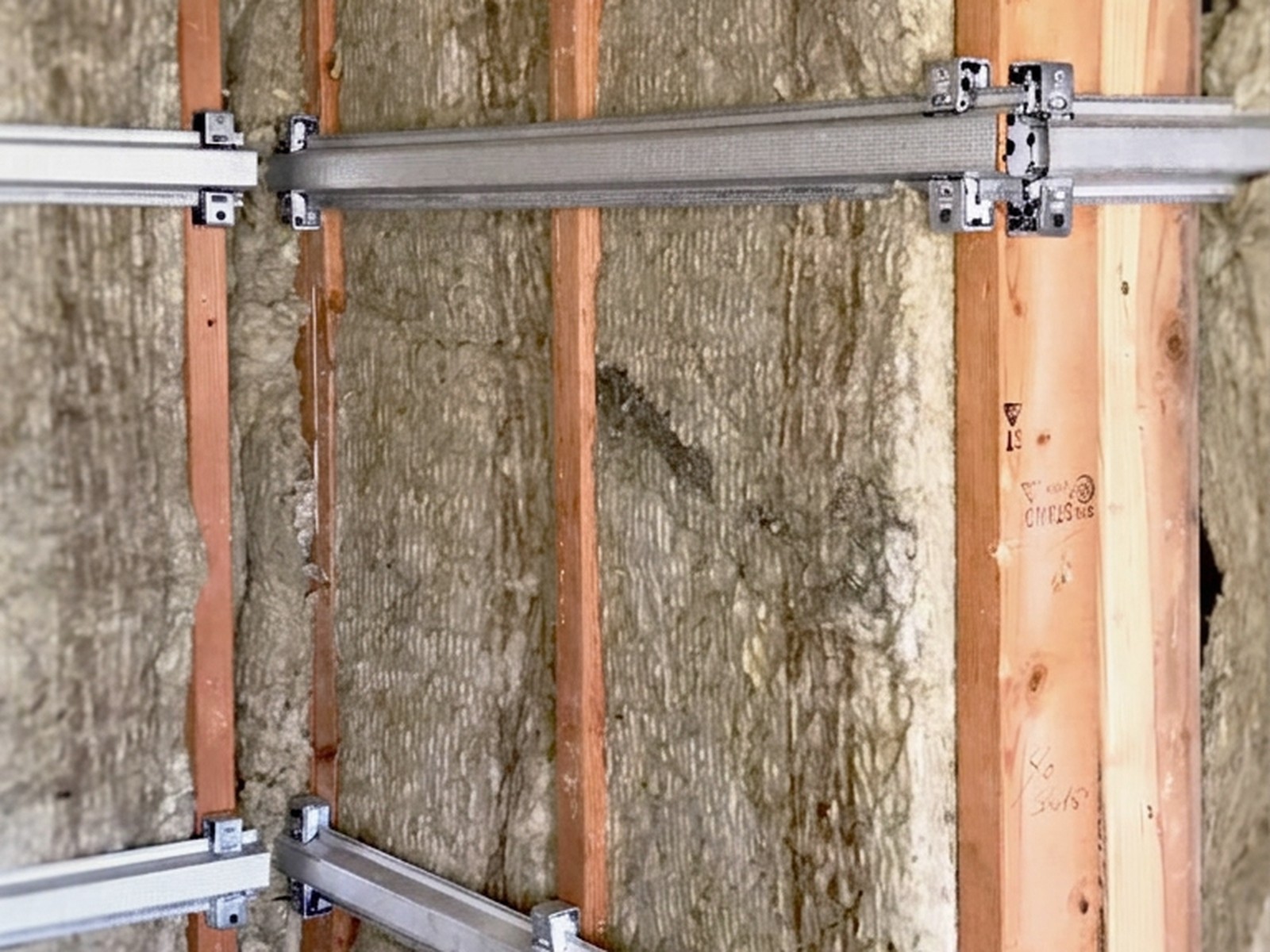 Sound isolation clips and hat channel installed over mineral wool insulation in a stud wall cavity — soundproofing acoustics services.