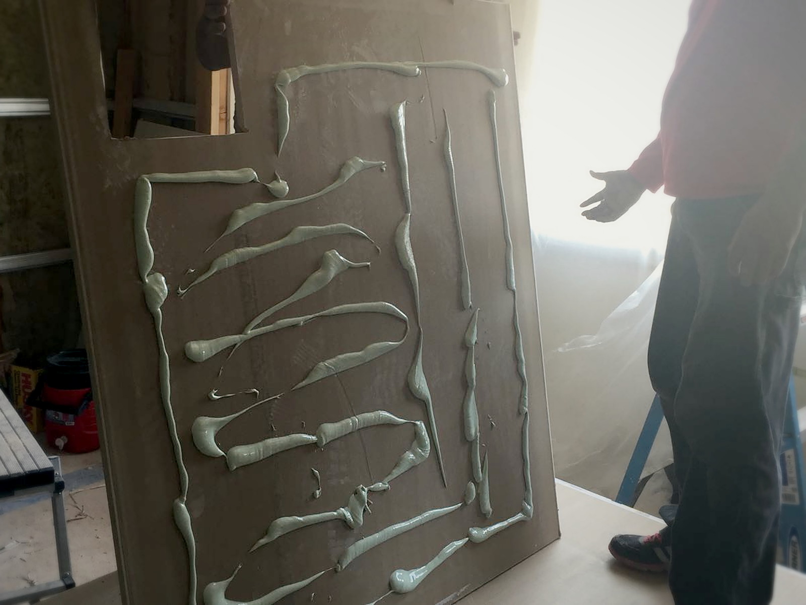 Green Glue damping compound applied in serpentine beads across the back of a drywall sheet before hanging