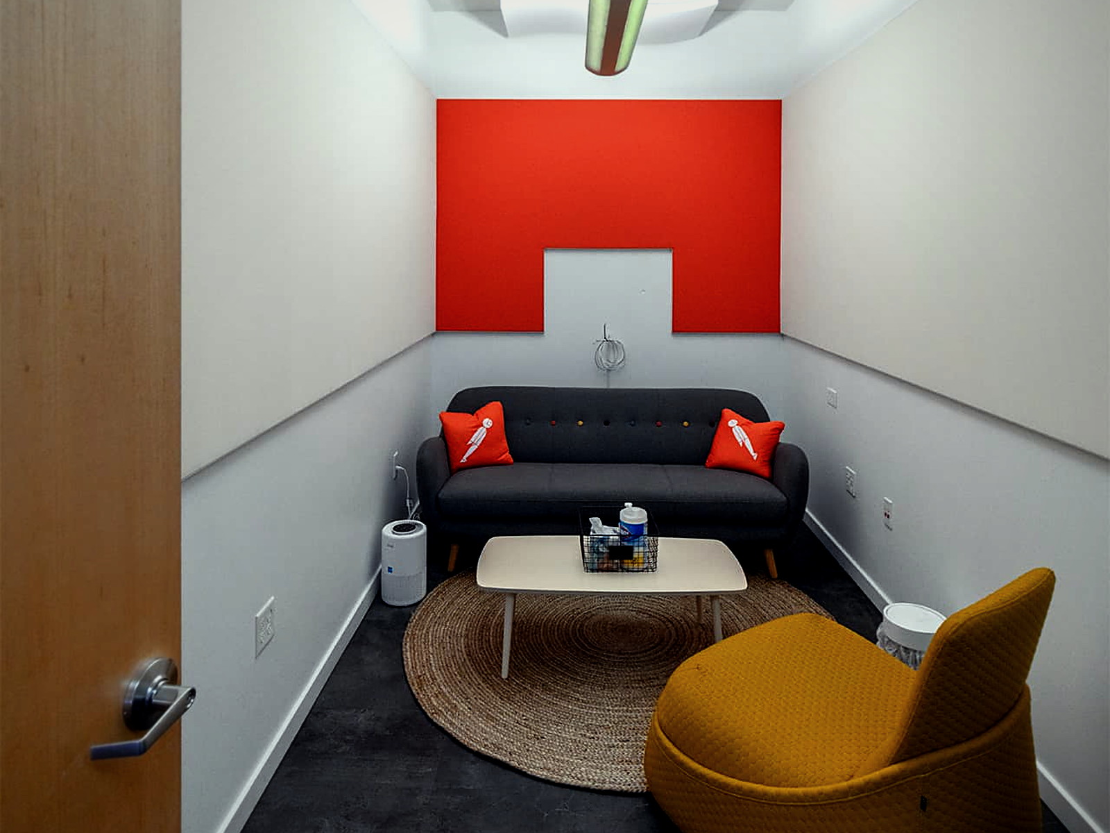 Small phone room with layered acoustic ceiling clouds above a sofa and lounge chair on an orange accent wall