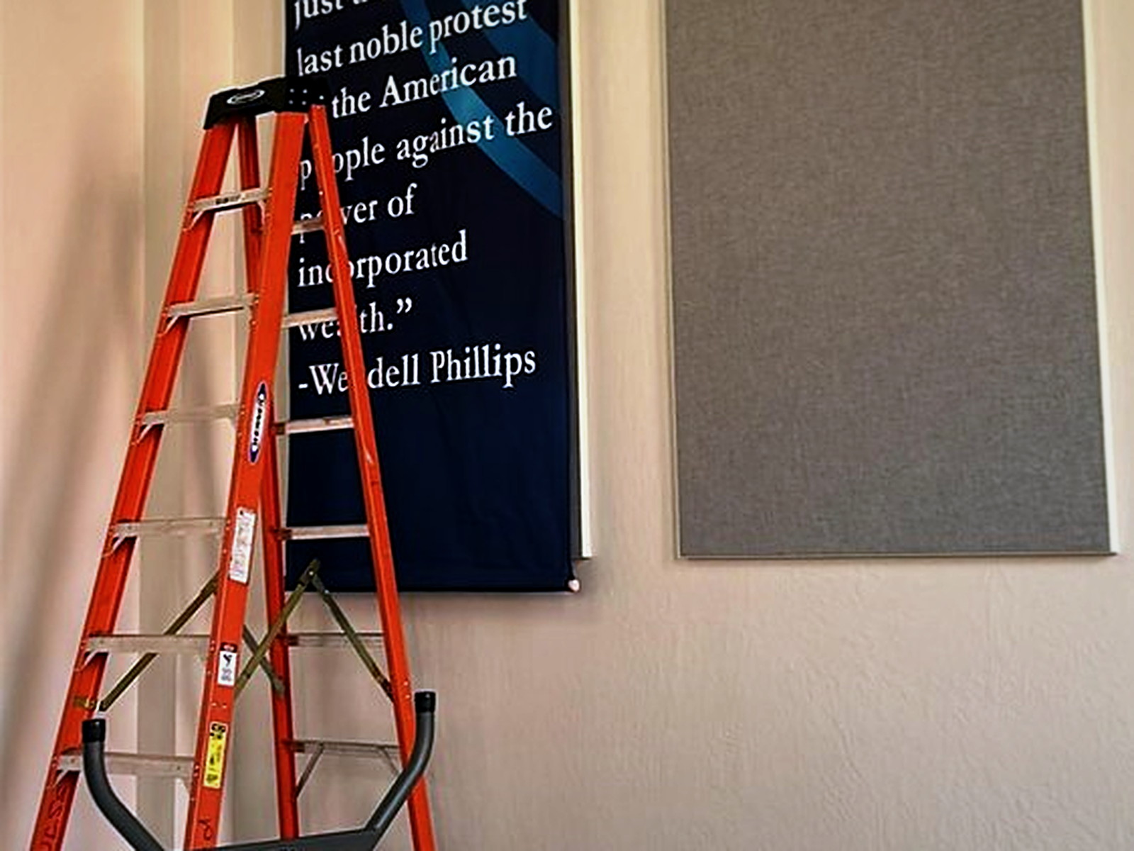 Institution wall banner being rehung on its rod directly over a finished custom fabric track acoustic panel
