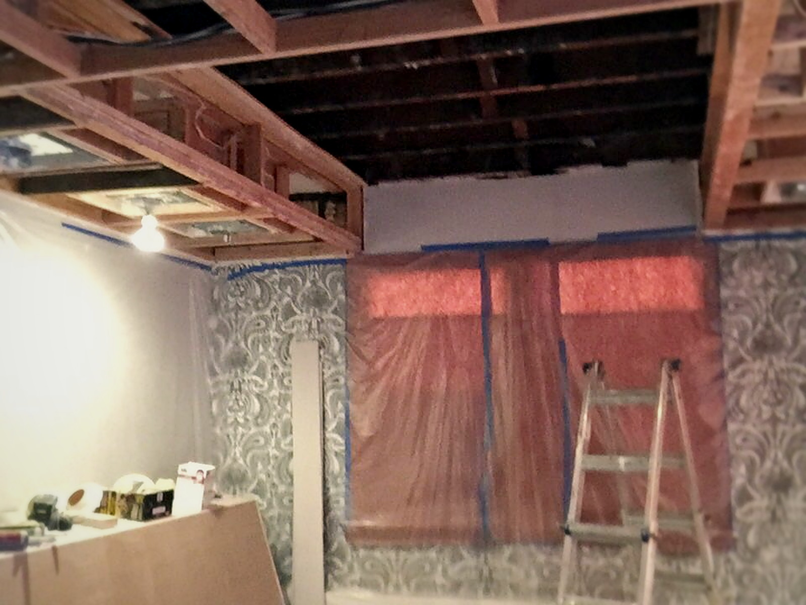 Ceiling joists exposed above a masked Melrose living room during soundproofing demolition