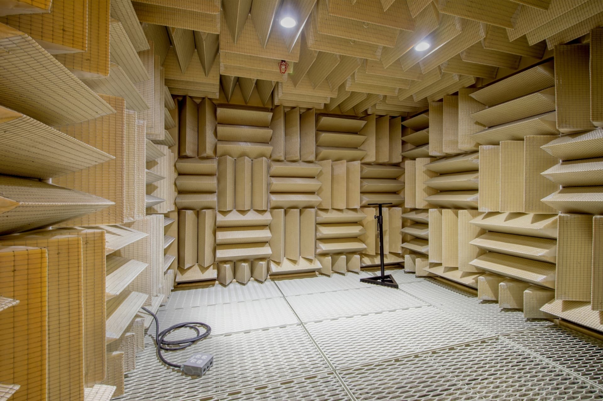 Acoustics test chamber lined floor-to-ceiling with anechoic foam wedges and a mic stand on the mesh floor — acoustic design and treatment services.