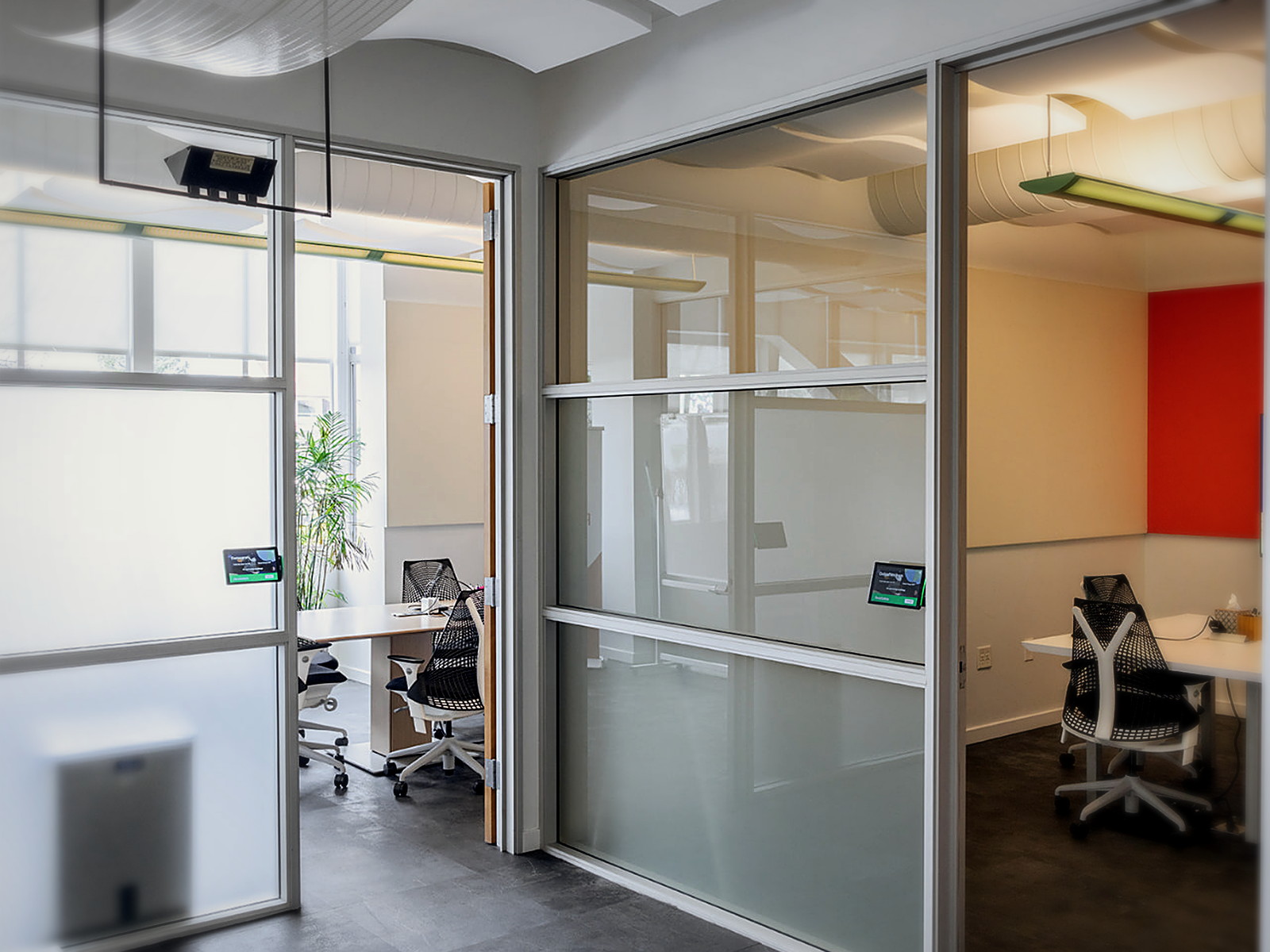 Glass-walled Berkeley office focus rooms with curved white acoustic ceiling clouds overhead and an orange accent wall