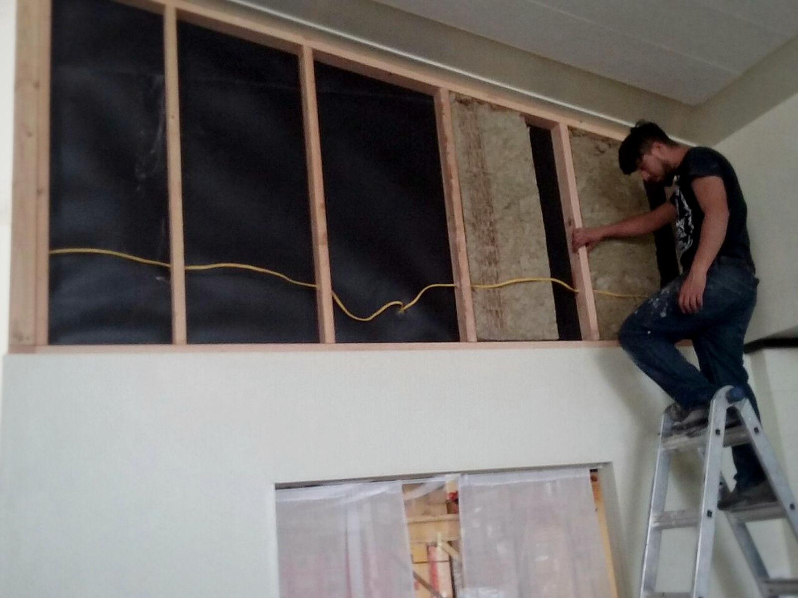 Installer fitting mass loaded vinyl over mineral wool insulation in a classroom transom infill wall