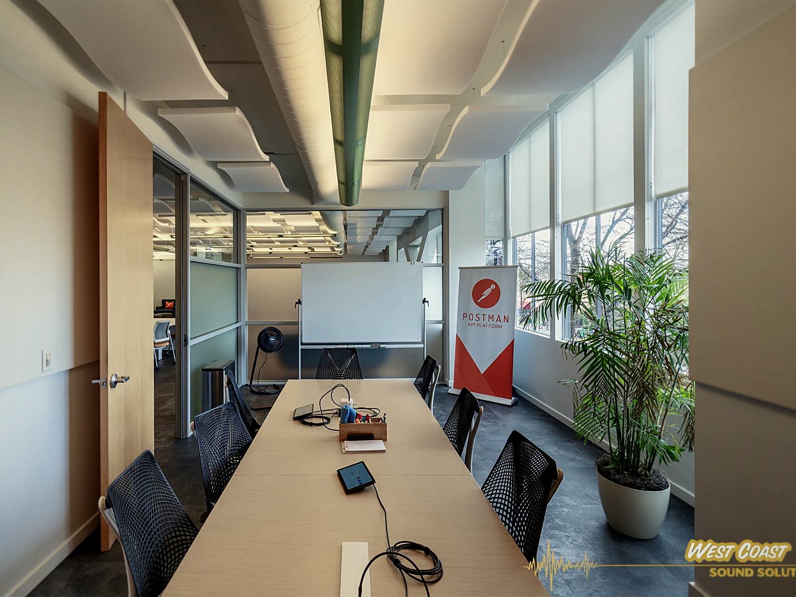 Long conference room in a Berkeley office with acoustic ceiling clouds above the table and daylight from a full window wall