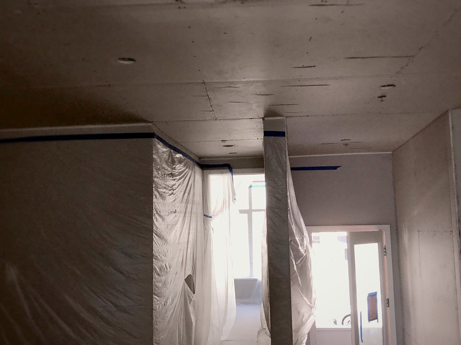 Newly hung drywall ceiling over a clip and channel soundproofing assembly in a masked San Francisco home